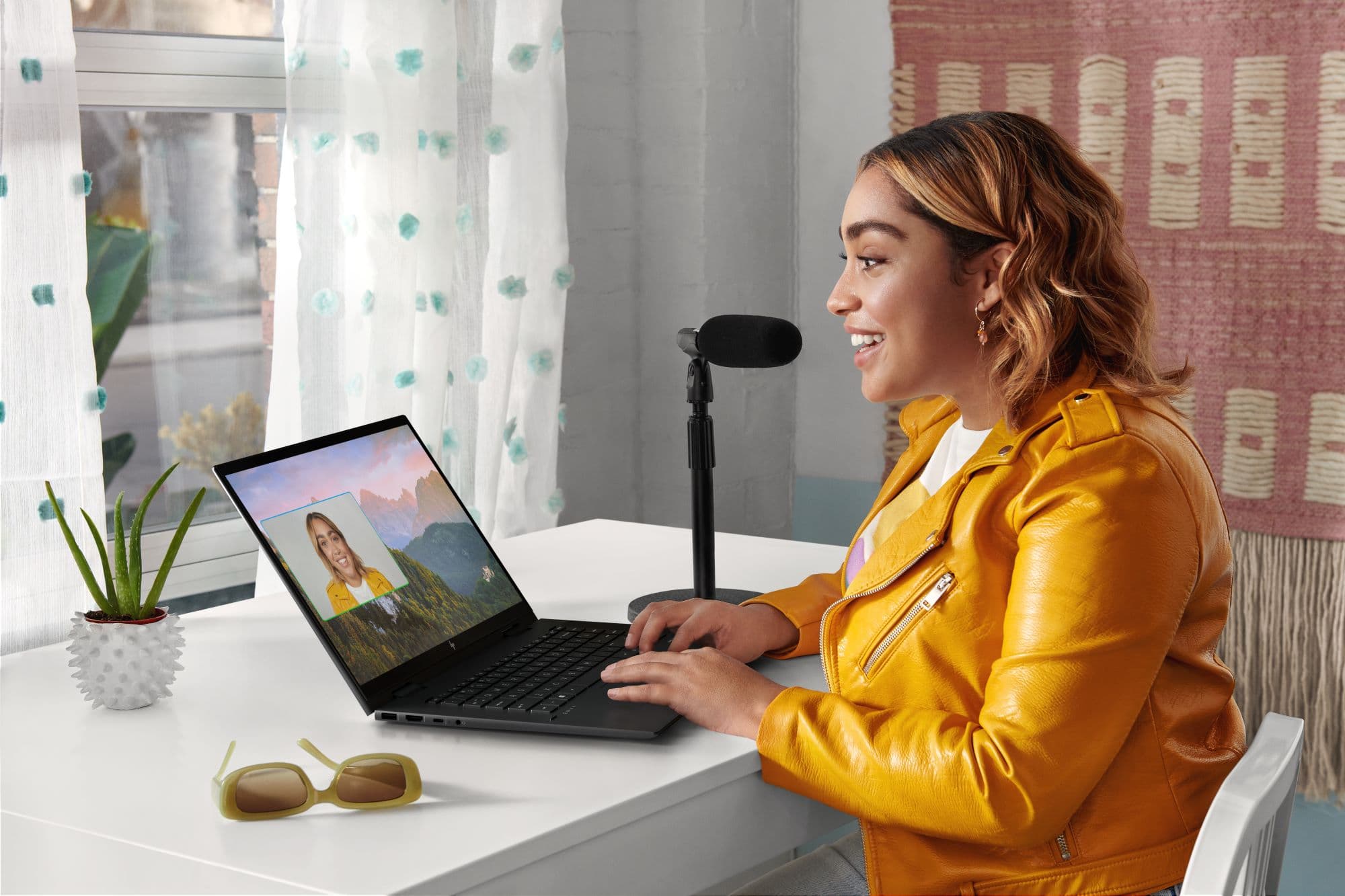 Young woman in a yellow jacket recording a video of herself using a sleek black HP laptop